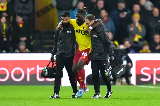 Watford's Festy Ebosele (centre) is helped off the field by medical staff after picking up an injury