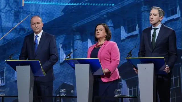 Three leaders - Micheál Martin, Simon Harris, Mary Lou McDonald standing behind podiums at the leaders debate.