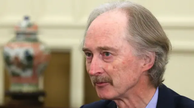 Geir O. Pedersen staring past the camera. He has greying, light brown hair and blue eyes, with a small moustache. He is wearing a suit.