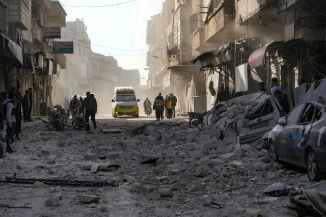 An ambulance rushes to the scene of a Syrian regime airforce strike which has left rubble all over the street and crushed cars