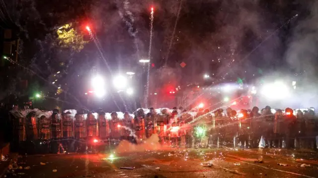 Fireworks burst brightly as they are launched towards a line of policemen on the street.