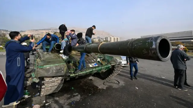 People pose for photos on an abandoned tank at Umayyad Square in Damascus on December 10, 2024