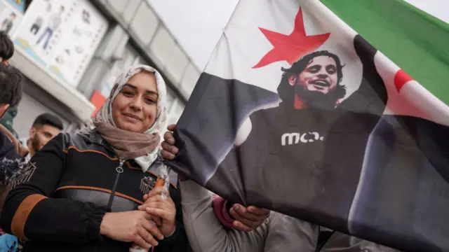 A Syrian woman in Ankara celebrates in the street, waving the new Syrian flag