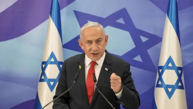 Prime Minister Benjamin Netanyahu stands at a podium with two Israeli flags draped behind him