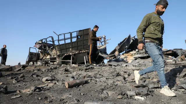 People gather around the damage by a burnt-out truck near Qamishli International Airport