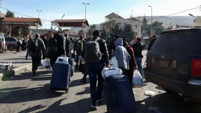 People walk with belongings as they attempt to cross into Syria, at the Masnaa border crossing between Lebanon and Syria