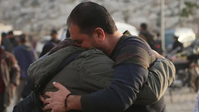 Two men hug tightly as other Syrians mill about them