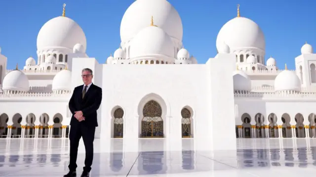 Starmer poses for a photo, smiling, in front of a white mosque with rounded turrets