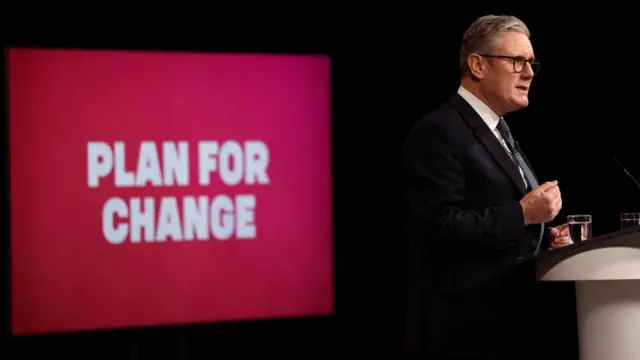 Starmer speals at a lectern, facing to the right. Behind him, on the left, is a red banner that reads 'plan for change'