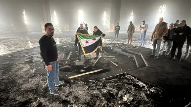 Rebel fighters stand with the flag of the revolution on the burnt gravesite of Syria's late president Hafez al-Assad at his mausoleum in the family's ancestral village of Qardaha