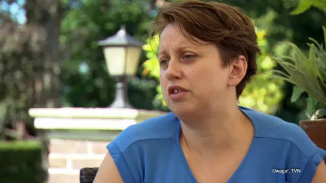 Sara's mother, Olga, sits in a garden and wears a blue T shirt. She is talking to the camera