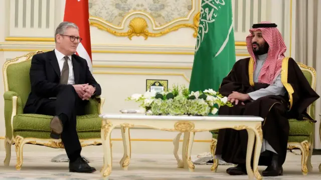 Starmer and MBS sit in green chairs with gold trimmings, facing a 45 degree angle, with their respective flags hanging behind them