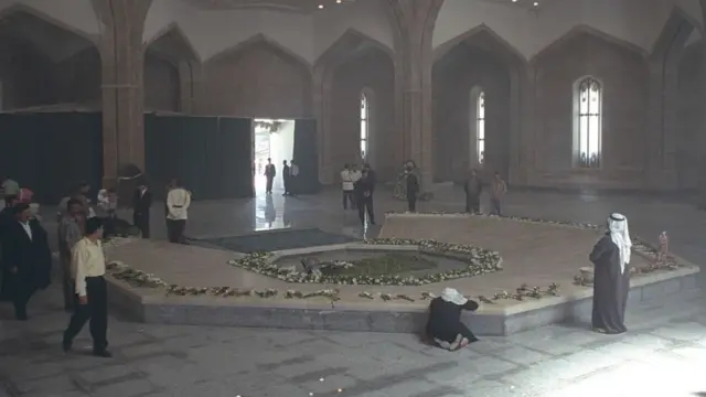 Hafez al-Assad mausoleumfollowing the former president's death, with floral tributes being laid by visitors. Several men can be seen walking around the coffin covered in flowers and greenery at the centre