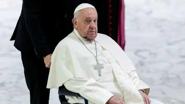 Pope Francis in a wheelchair with a large bruise on his chin