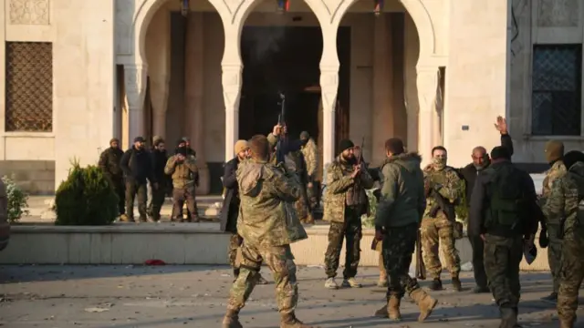 A dozen opposition fighters fire their guns in the air in celebration in front of a Syrian government