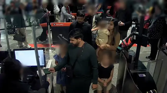 CCTV images of three adults standing at passport control. They are standing with children, whose faces are blurred