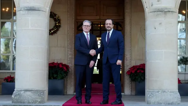 Starmer and Christodoulides shake hands in front of a large wooden door, between two sandstone columns