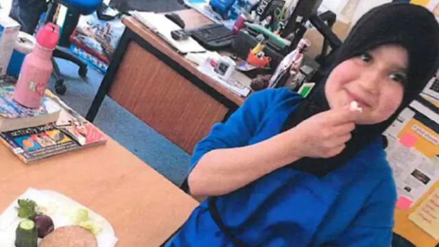 A picture of Sara wearing a blue outfit and a head covering eating next to a desk