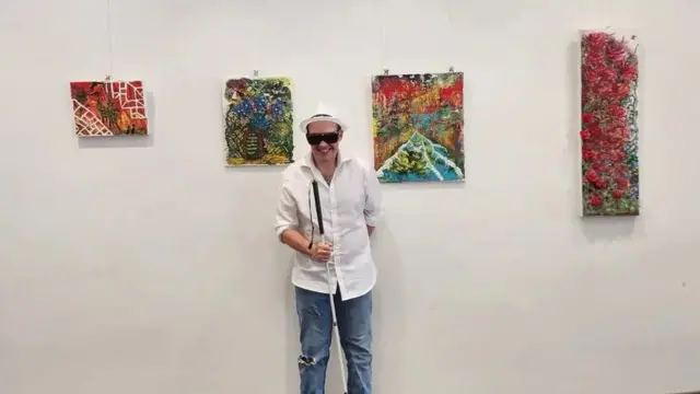 Adrian stands in front of four pieces of his work