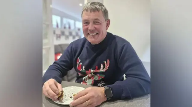 Man in Christmas jumper smiling whilst holding mince pie