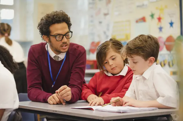 Two schoolboys work through a textbook with their teacher
