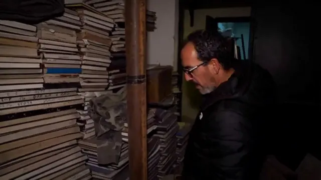 Man looks at piles of old and aged books stacked up to the ceiling of building