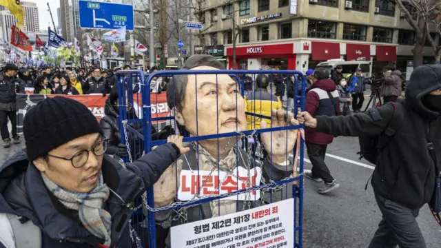 People pushing a cage containing an effigy of President Yoon