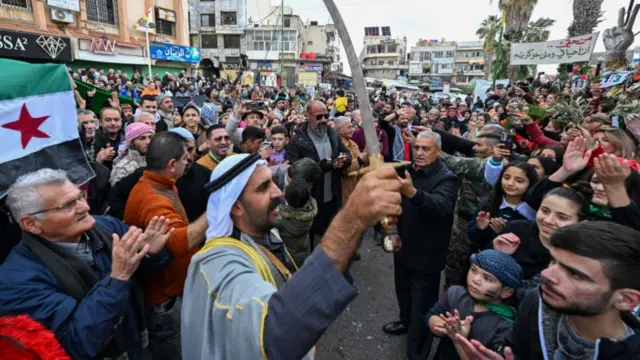 Man holding sword up as huge crowd round him claps