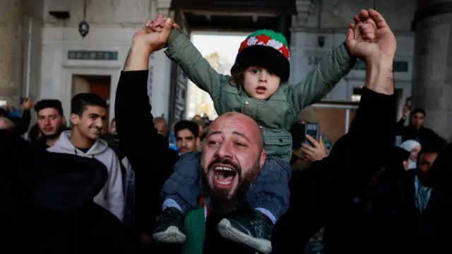 Jubilant man holds young child on his shoulders with both of their arms raised in the air