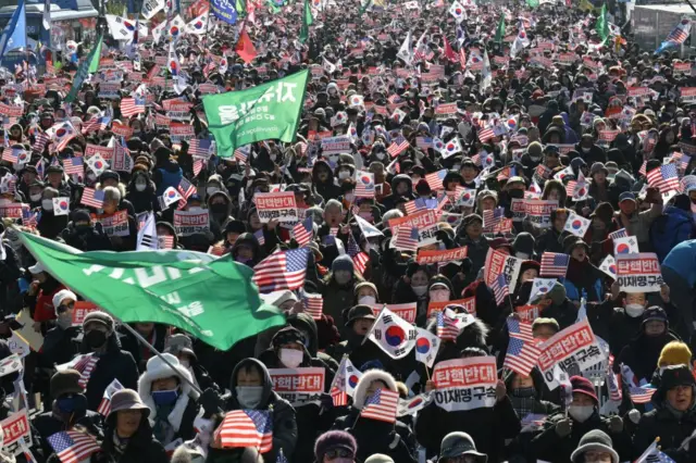 People wave flags of South Korea and the United States as they hold signs reading "Against impeachment... arrest Lee Jae-myung"