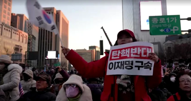 A Yoon supporter waving the South Korean flag and holding a sign which reads "Oppose impeachment. Arrest Lee Jae-Myung."