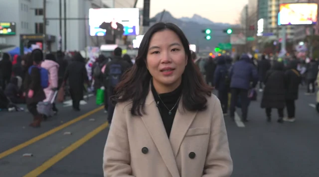 Yuna Ku stands on a road in front of groups of pro-Yoon supporters