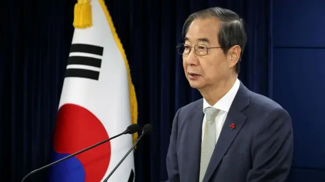 Acting president Han Duck-soo speaking at microphone with South Korean flag in background