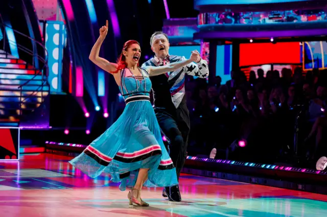 Dianne pointing her finger in the air while on the dancefloor as Chris leads the pair forward