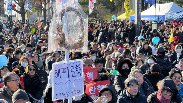 A man sitting in a crowd, holding a stick with a sign attached to it