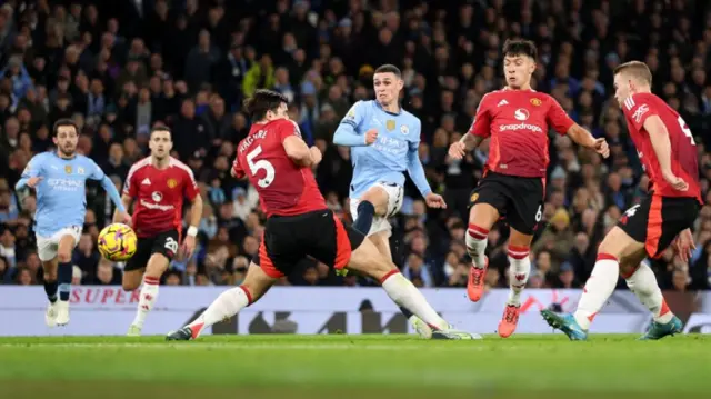 Phil Foden of Manchester City shoots whilst under pressure from Harry Maguire and Lisandro Martinez