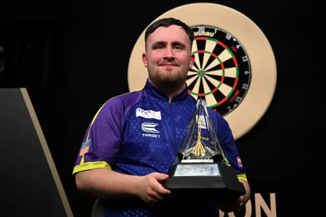 Luke Littler holding his 2024 Premier League trophy