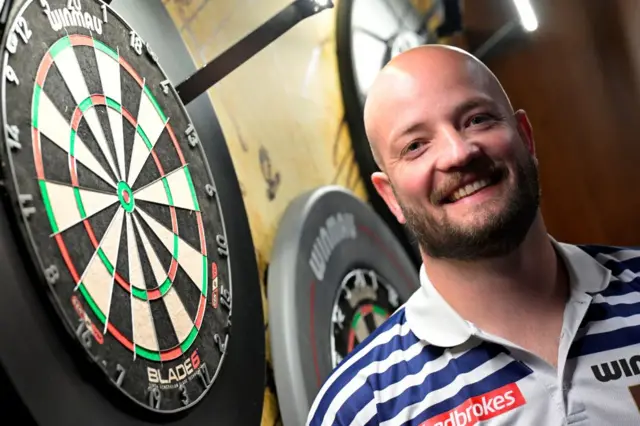 Thibault Tricole smiles next to a dart board