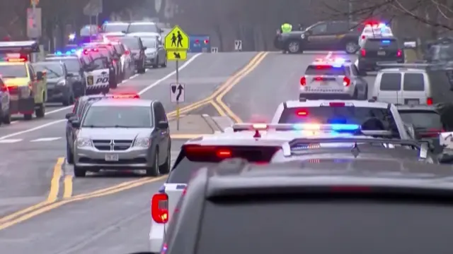 Cars line the road outside a Winsconsin school. Numerous vehicles with flashing lights can be seen