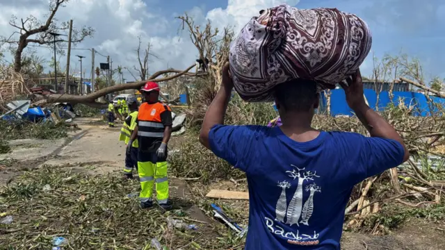 A man carries his belongings as rescue workers attempt to clear a blocked road, in the aftermath of Cyclone Chido, within Labattoir, in Mayotte, France, December 15, 2024
