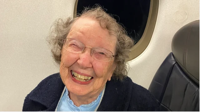 Patricia smiling at the camera sat at a window seat of an airplane