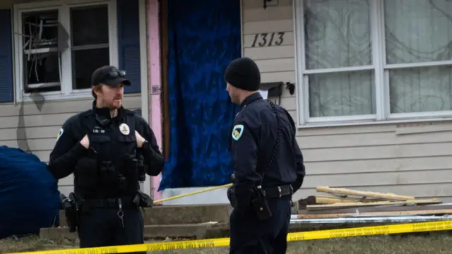 Police stand outside the damaged home of the shooter