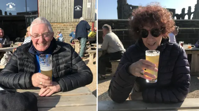 A composite image of two people sat outside drinking beers. On the left is a man with grey hair and a black coat, on the right a woman with curly hair and a purple coat.