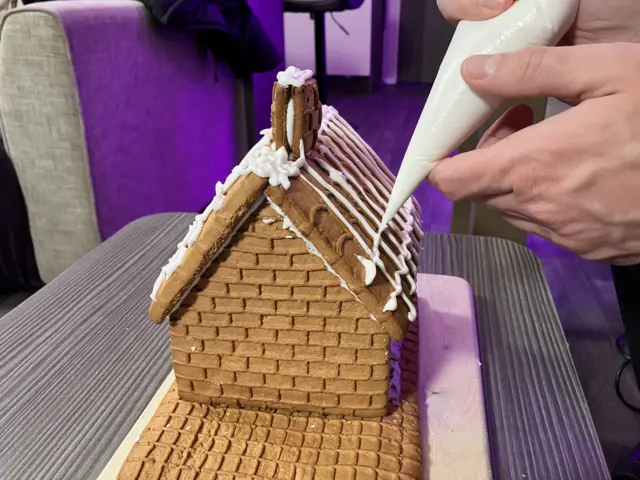 Charlie Taylor's hand pipes icing onto a gingerbread house