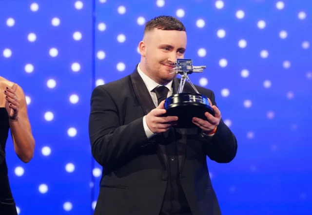 Luke Littler holds his trophy