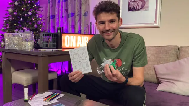 Charlie Taylor holding Christmas cards in one hand and decorations in the other