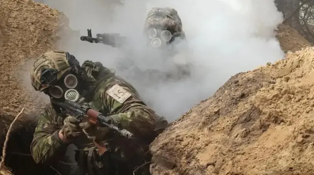 A Ukrainian soldier wearing a gas mask firing a gun