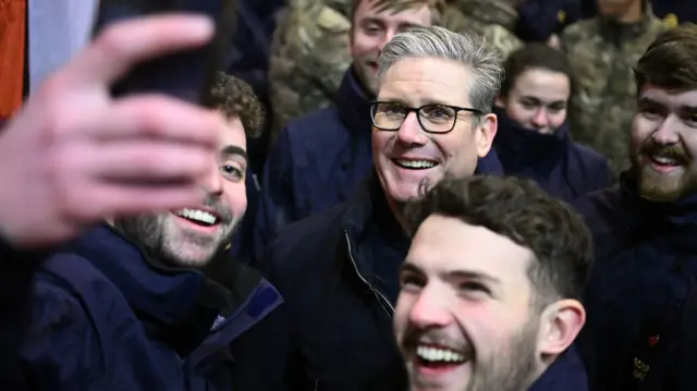 A man takes a selfie on a mobile phone with Starmer smiling at the centre of a group of people