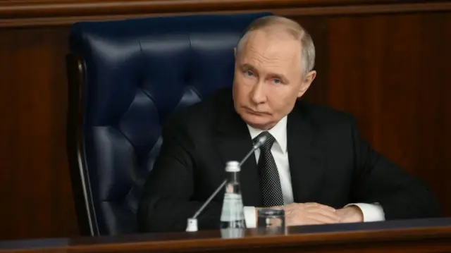 Russian President Vladimir Putin sits at a desk and listens.