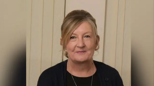 Sue Craft smiles at the camera; she's wearing a black top and  a necklace